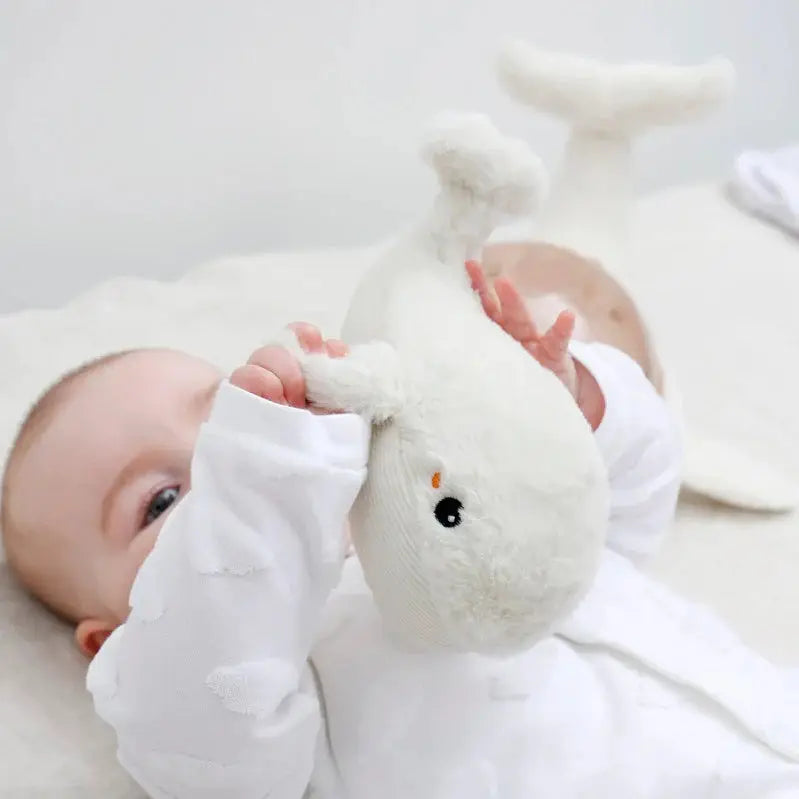 Glückliches Baby liegt auf Bett und spielt mit weichem Kuscheltier Spielzeug für Babys zur Förderung der Entwicklung