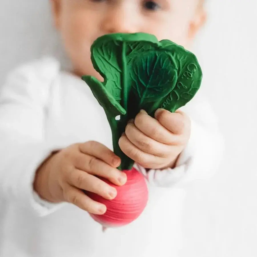 Baby hält grünen Beißring in Form eines Radieschens aus natürlichen Materialien Rasseln und Beißringe