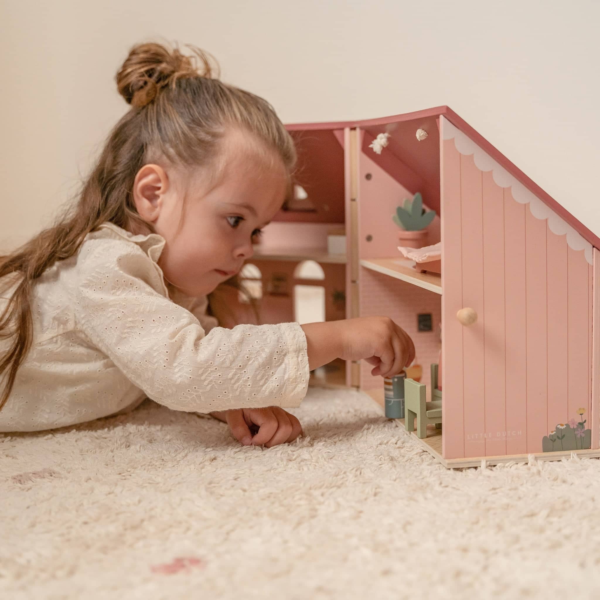 Spielzeug ab 3 Jahren mit Mädchen, das ein rosa Puppenhaus auf einem Teppich spielt
