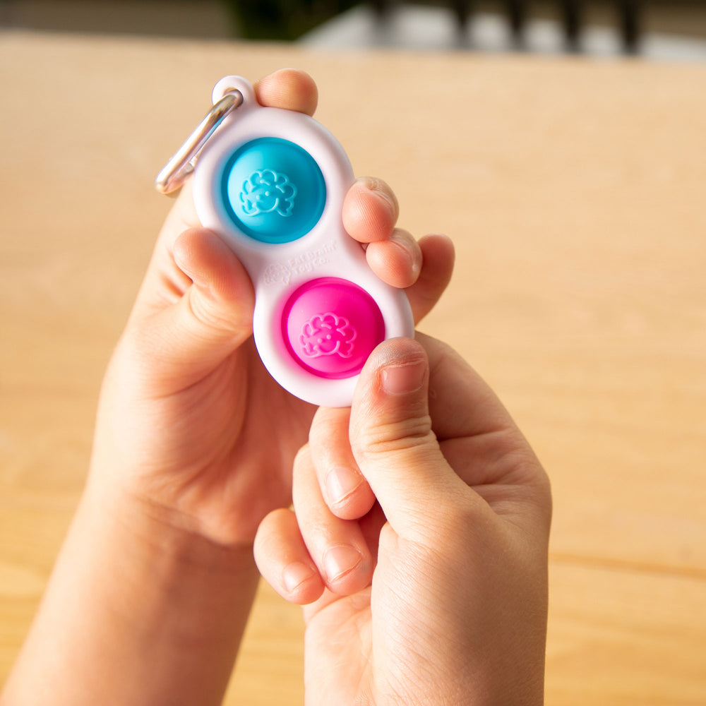 Eine Hand hält den Dimpl Blasen Schlüsselanhänger von Fat Brain Toys zum Drücken und Spielen. Dimpl Blasen Schlüsselanhänger kaufen.