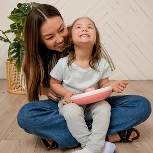 Großer Snackbehälter Snack Spinner – Coral Pink in der Hand eines lächelnden Kindes mit Mutter im Hintergrund