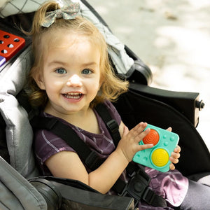 Fat Brain Toys Schubblasen-Tastplatte in der Hand eines fröhlichen Mädchens im Kinderwagen