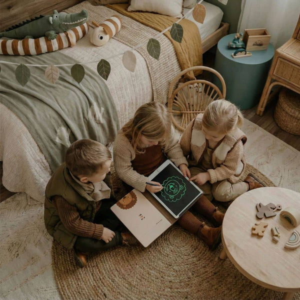 Kinder, die zusammen mit einem Grafiktablett für Kinder in einem gemütlichen Raum zeichnen