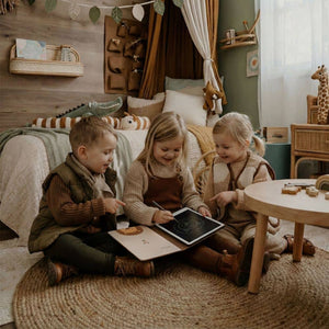 Drei Kinder zeichnen mit einem Grafiktablett für Kinder in einem gemütlichen Raum voller Spielzeug.