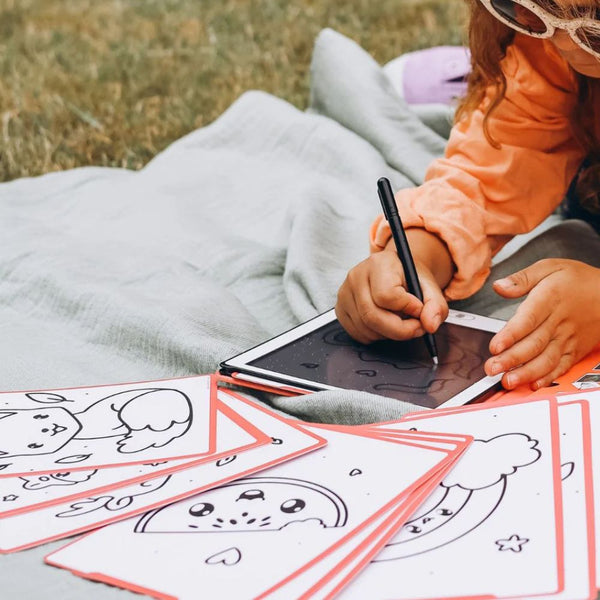 Kind malt mit Grafiktablett Kidydraw Mini – Kawai auf einer Decke im Freien