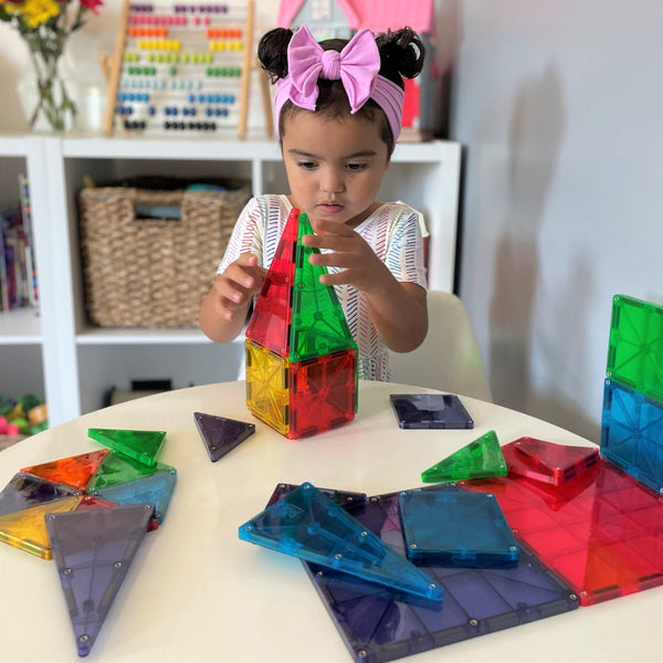 Ein Kind baut mit bunten Magnetbausteinen Kinder von MAGNA-TILES auf einem Tisch