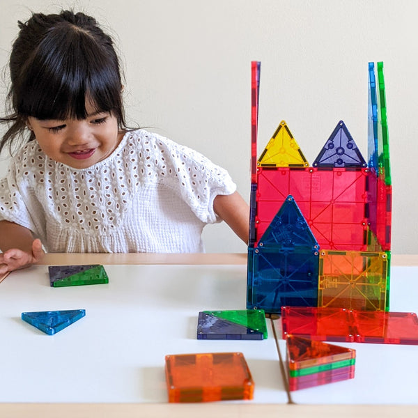 Ein Kind spielt mit MAGNA-TILES Magnetbausteine Kinder und baut bunte Strukturen auf einem Tisch