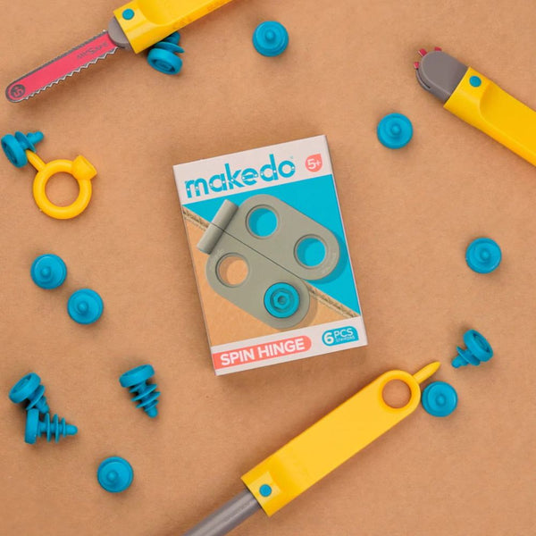 Makedo Spin-Scharnier-Set 6-tlg. mit gelben Werkzeugen und blauen Verbindungselementen auf braunem Untergrund