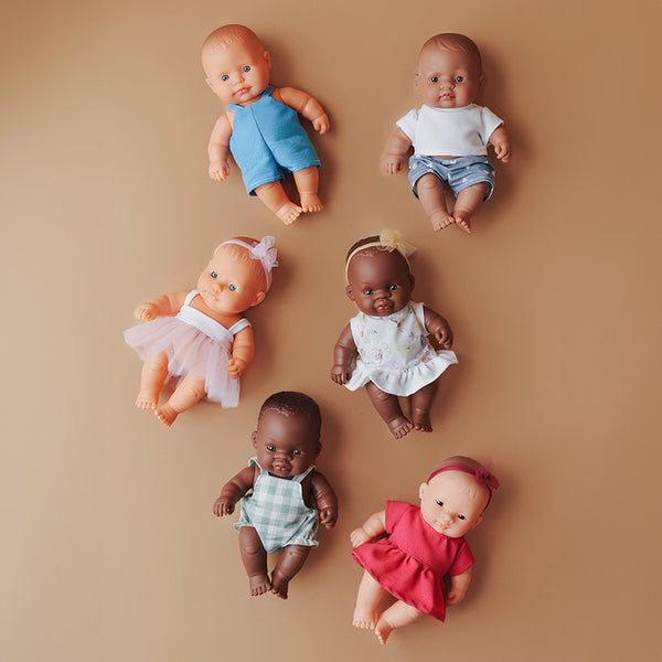 Miniland Puppen-Set mit sechs verschiedenen Baby-Puppen in bunten Kleidern auf beigem Hintergrund