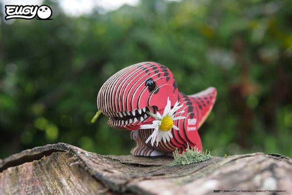 Eugy Öko 3D Puzzle Tyrannosaurus in lebendigen Farben mit einer Blume im Mund auf einem Baumstamm