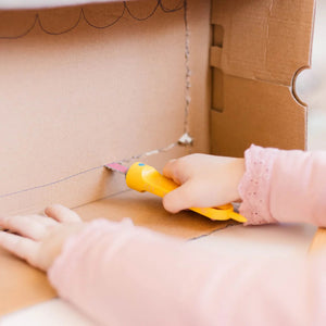 Kind benutzt die Makedo Sichere Säge - Safe-Saw zum Schneiden von Karton in gelbem Werkzeuggriff