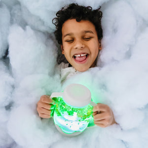 Kind hält Sensorik-Glas zum Befüllen mit Wasser – grau von Glo Pals, umgeben von weichem Material