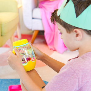 Kind hält ein gelbes Sensorik-Glas zum Befüllen mit Wasser – gelb von Glo Pals in der Hand