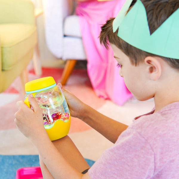 Kind hält ein gelbes Sensorik-Glas zum Befüllen mit Wasser – gelb von Glo Pals in der Hand