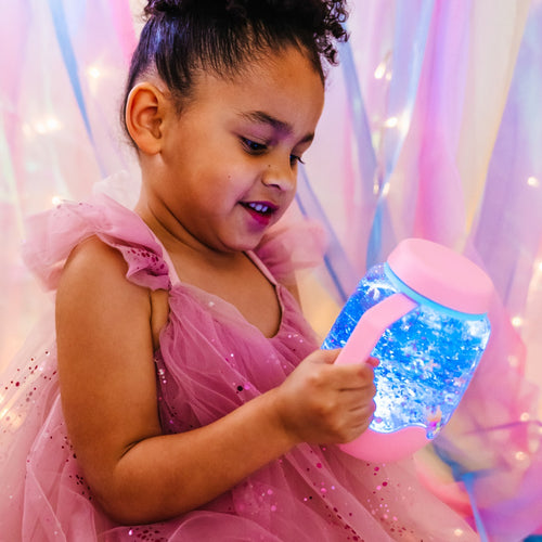Mädchen spielt mit dem Sensorikglas zum Befüllen mit Wasser – rosa von Glo Pals in einem leuchtenden Zimmer