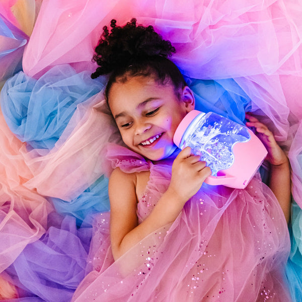 Kind liegt auf buntem Stoff und hält ein Sensorikglas zum Befüllen mit Wasser – rosa von Glo Pals