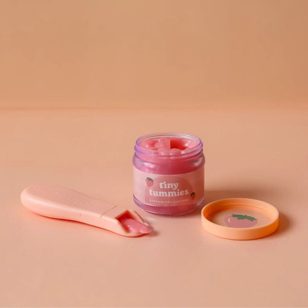 Puppen Fütterungsset mit Löffel von Tiny Harlow, bestehend aus Lippenpflegedose und Löffel auf einem sanften Hintergrund